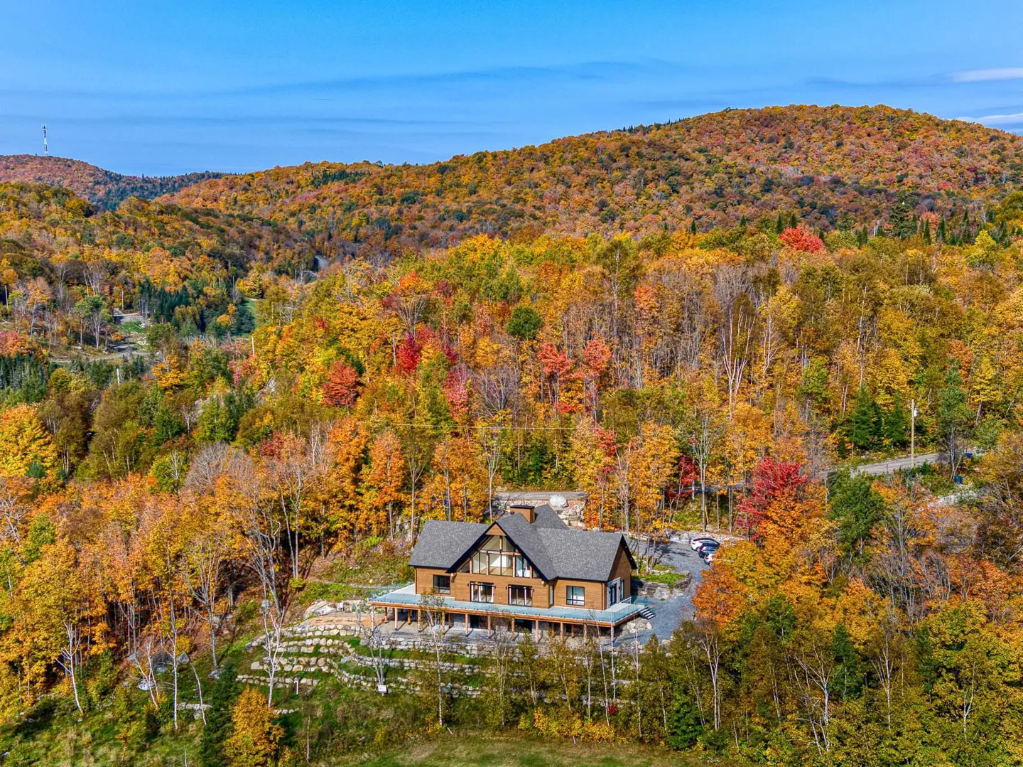 A brown house with a gray roof sits on a hill surrounded by colorful autumn trees.