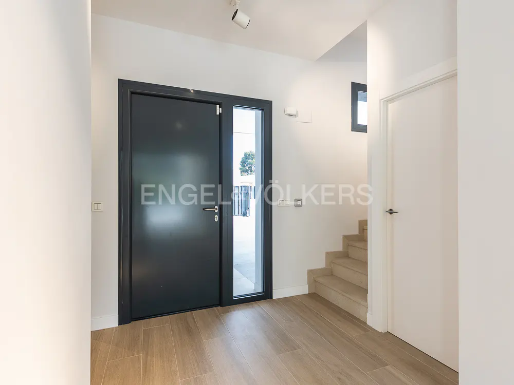 Modern home entryway with a dark gray front door, light wood floors, and white walls. Stairs lead to the upper level.