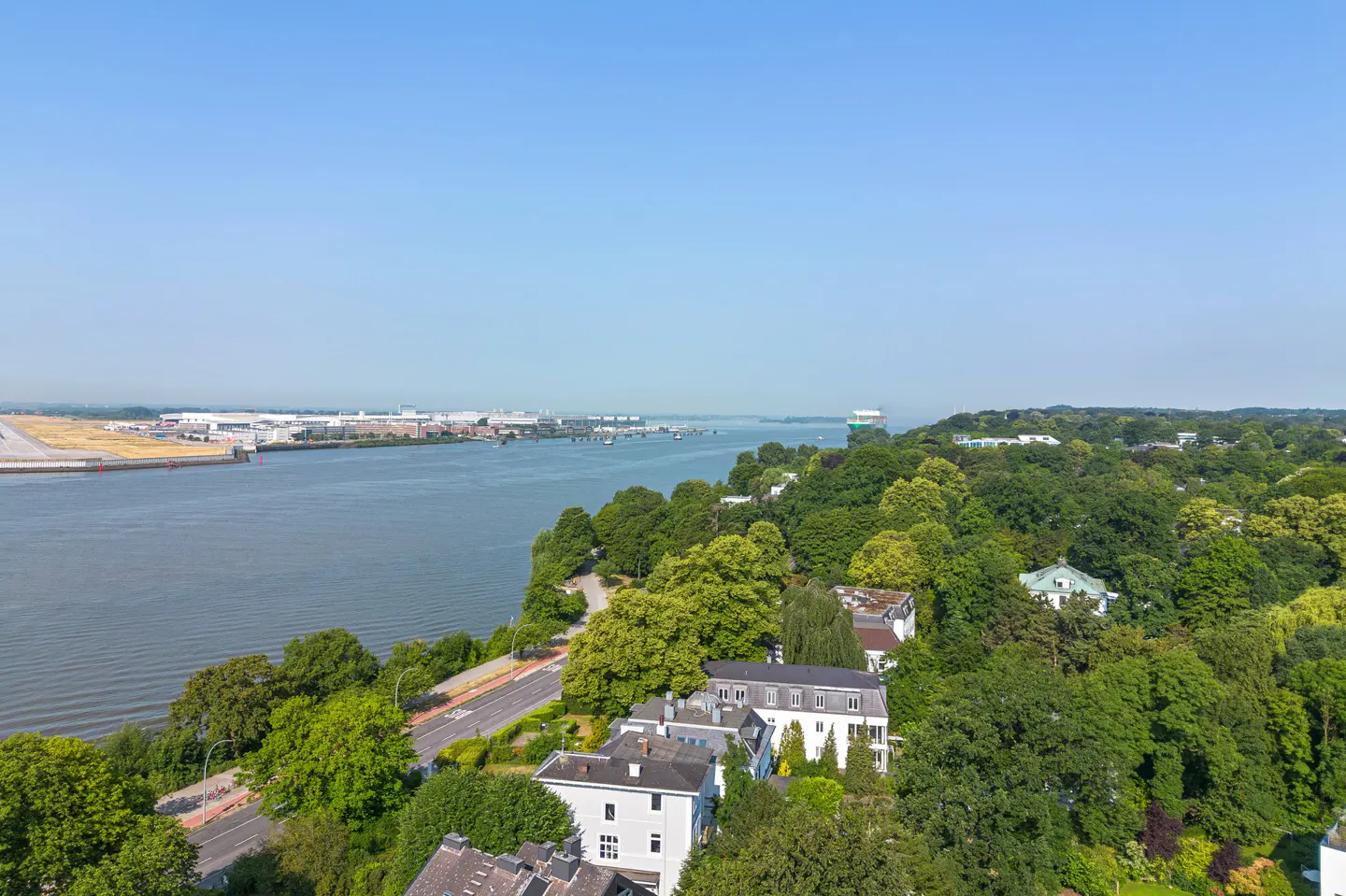 Aerial view of Elbe river, Hamburg, Germany, with lush green trees, white houses, and blue sky.