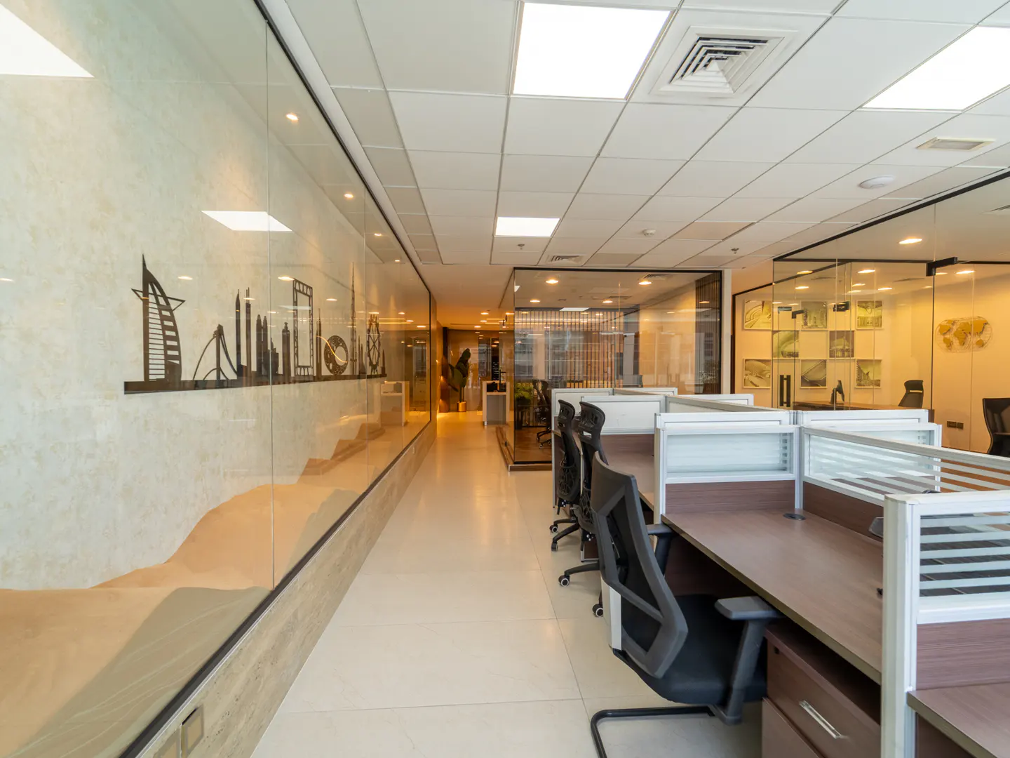 Bright office space with cubicles and glass walls. A Dubai skyline graphic adorns the wall.