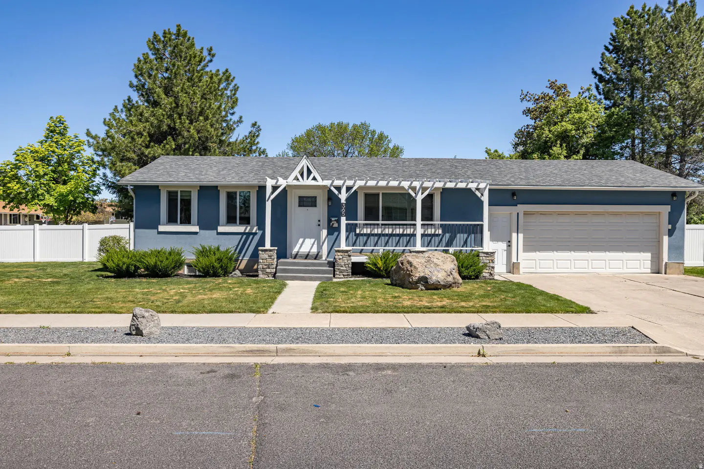 Blue single-story house with white trim, a white pergola over the porch, and a gray roof on a sunny day.