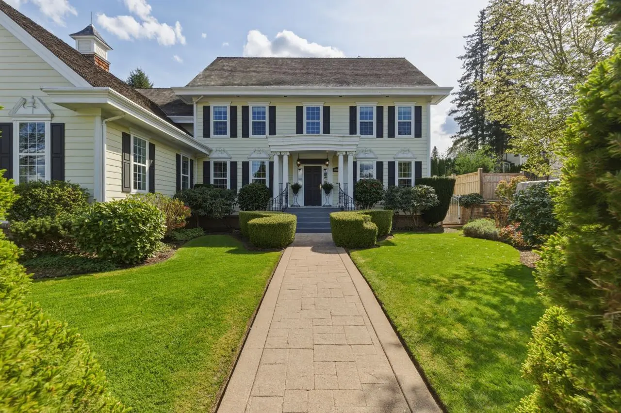 Two-story pale yellow house with black shutters, a stone walkway, and manicured green lawn.