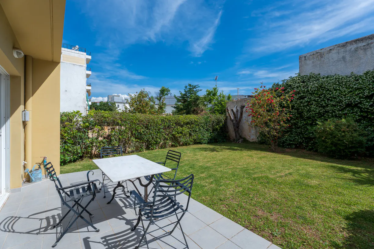 Outdoor patio with a white table and four black chairs, green lawn, and blue sky.
