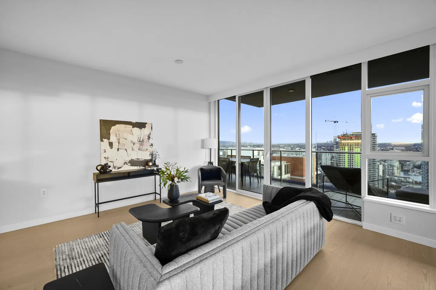 Bright living room with a gray sofa, black pillows, and a view of the city skyline through large windows.