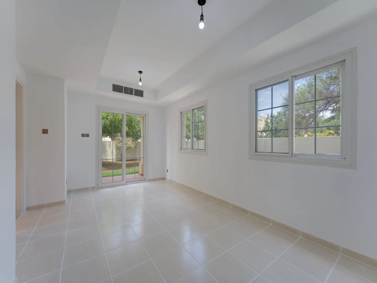 Bright, empty room with white walls, tile floor, and two windows. Sliding glass doors lead to a green yard.