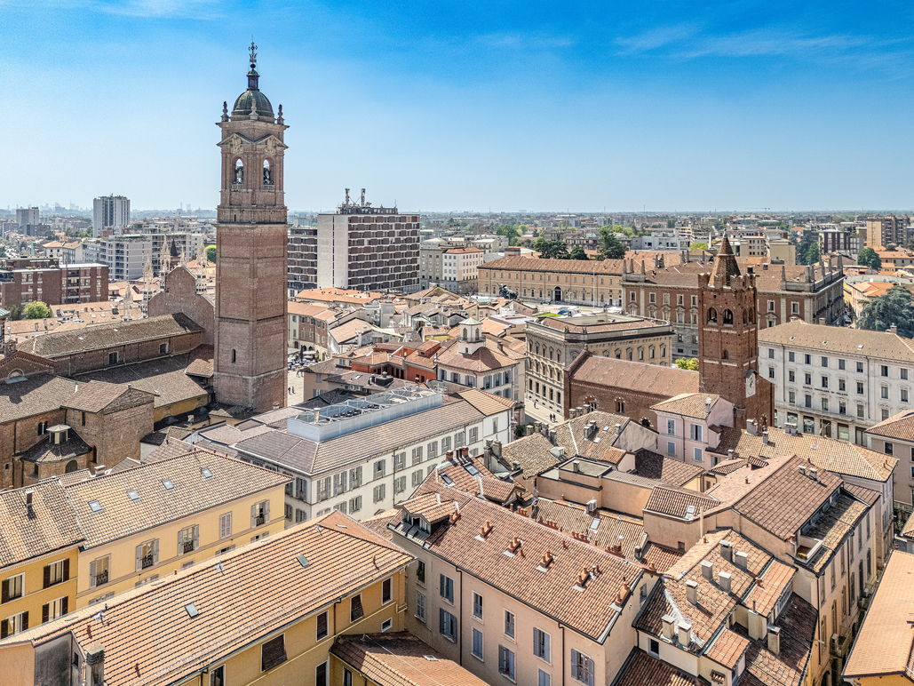 Aerial view of Mantua, Italy, featuring red-tiled roofs, brick towers, and a clear blue sky.