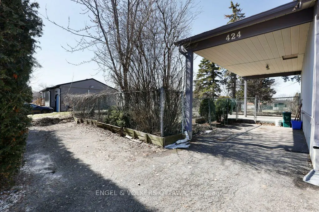 Exterior view of a house with a carport labeled "424", a gravel driveway, and a chain-link fence.