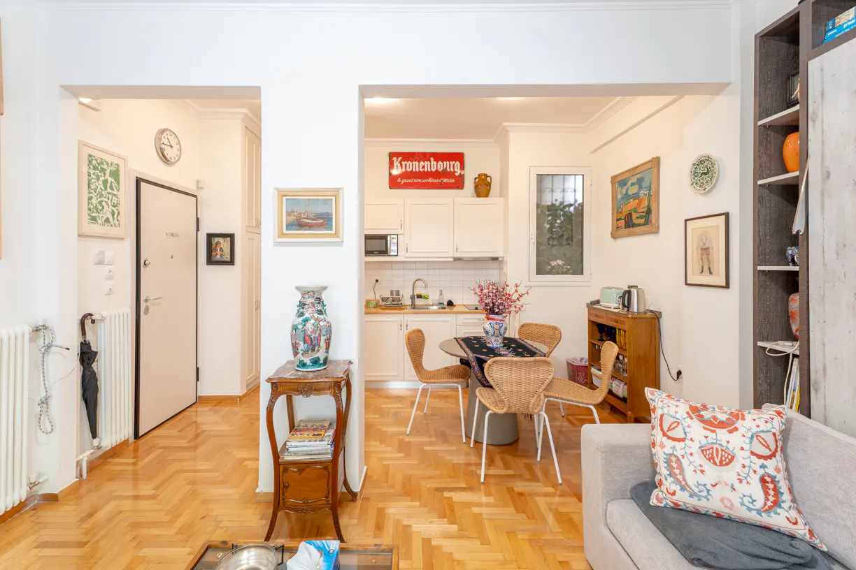 Interior view of an apartment with herringbone wood floors, white walls, and an open kitchen with a Kronenbourg sign.
