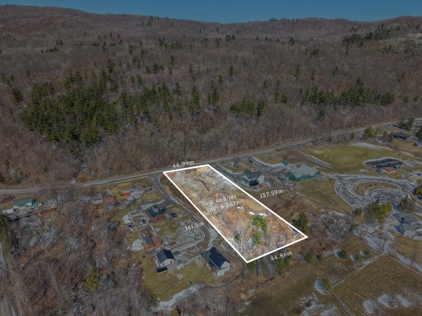 Aerial view of a vacant lot outlined in white, surrounded by houses and trees, with a mountain in the background.