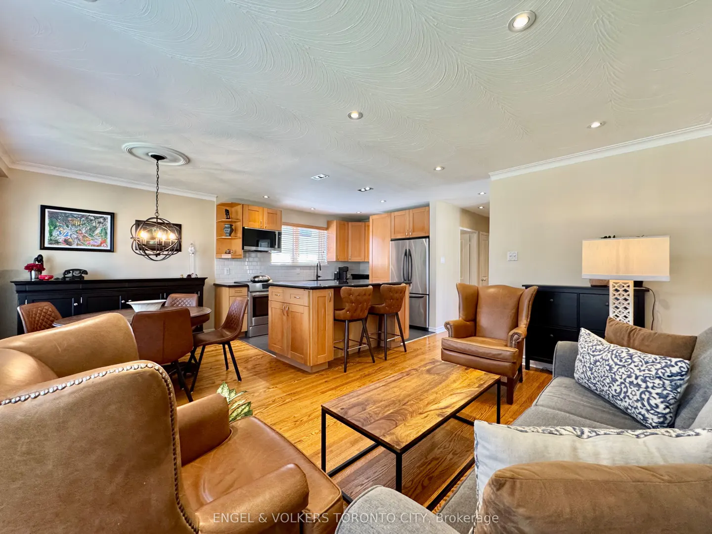 Open-concept living space with wood floors, featuring a kitchen island, leather chairs, and a gray sofa.