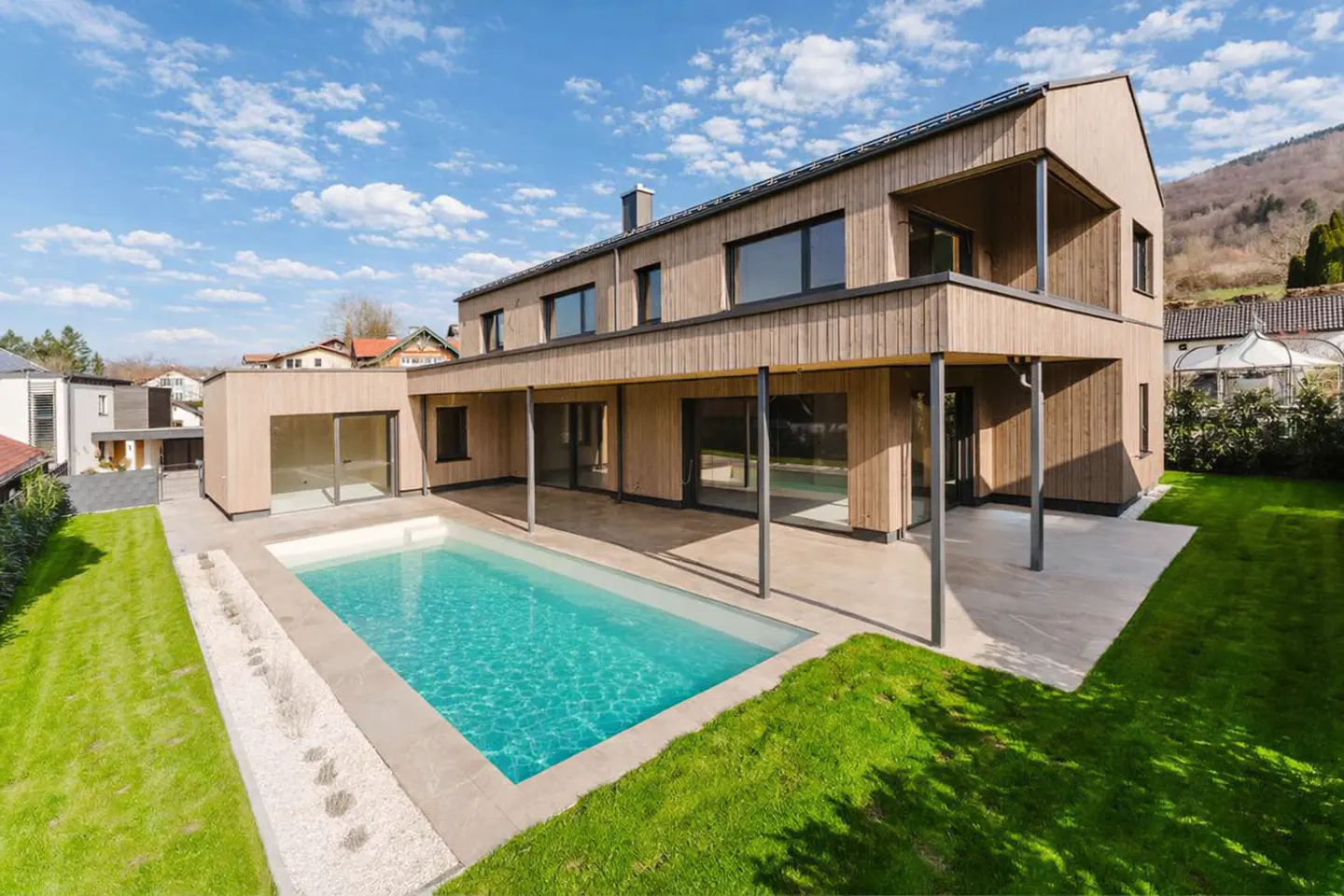 Two-story modern house with wood siding, a pool, and a green lawn on a sunny day.