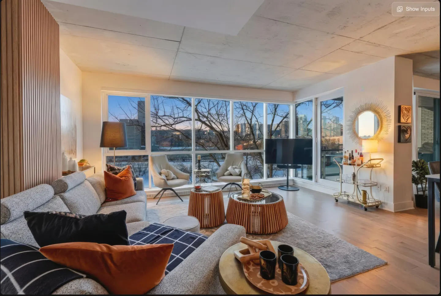 Bright living room with a gray sofa, orange pillows, and a view of the city skyline through large windows.