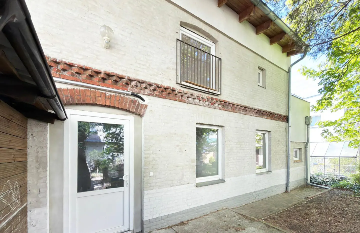 Exterior view of a two-story building with white brick, red brick accents, windows, and a white door.