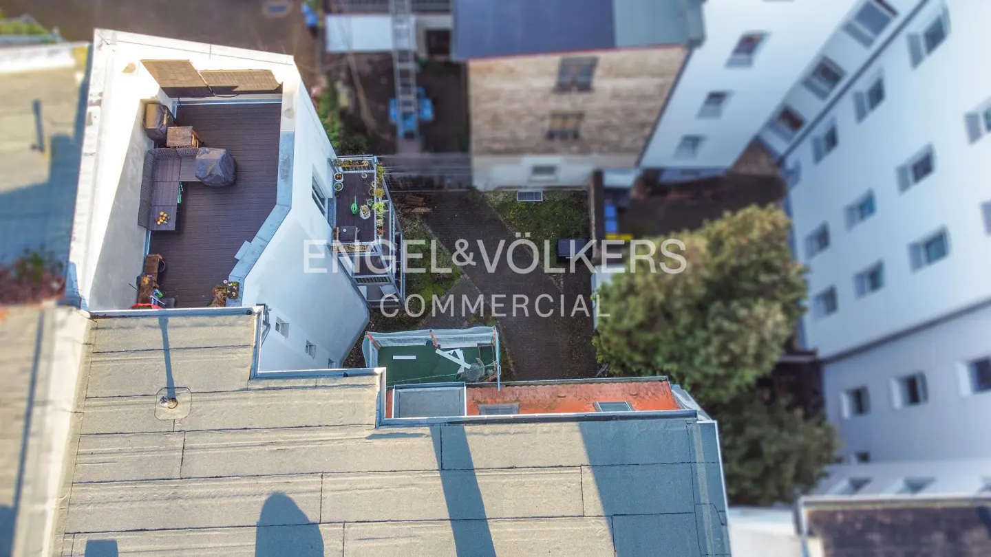 Aerial view of a building with a rooftop deck featuring outdoor furniture, a small garden, and the Engel & Völkers Commercial logo.