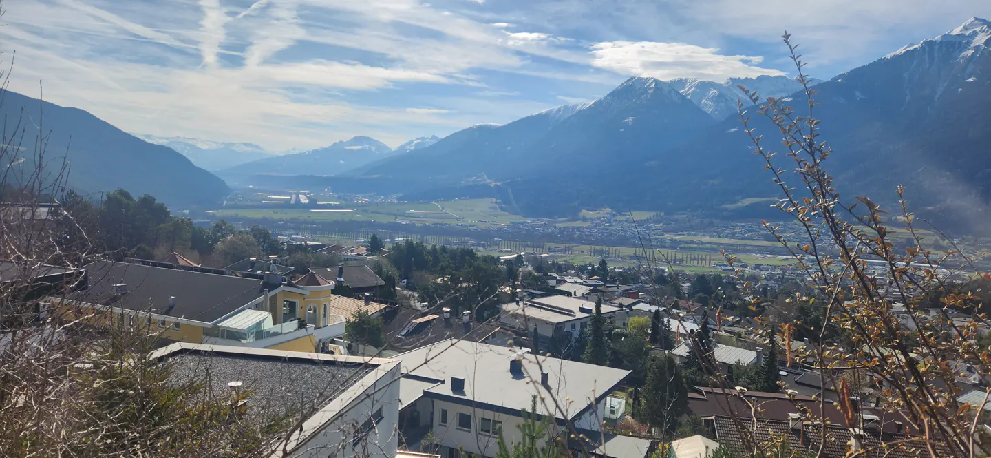 Scenic view of a town nestled in a valley, with snow-capped mountains in the background under a blue sky.