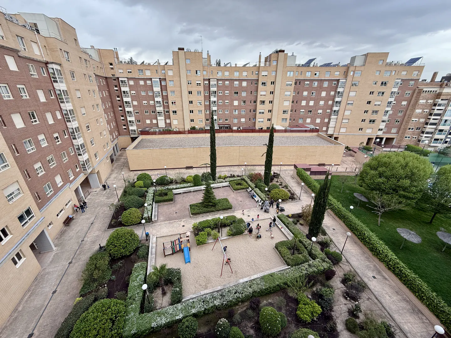 Aerial view of a courtyard with a playground, surrounded by brick apartment buildings under a cloudy sky.