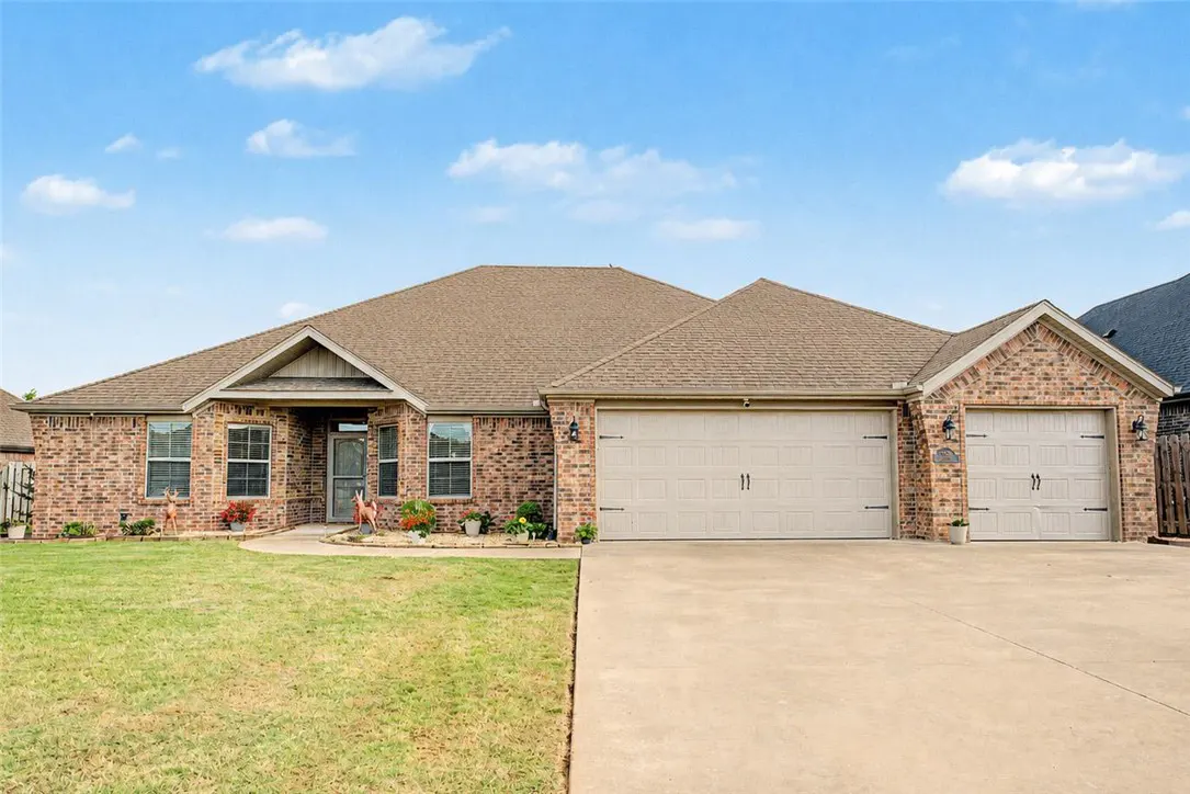 Single-story brick house with a brown roof, a two-car garage, and a green lawn under a blue sky.