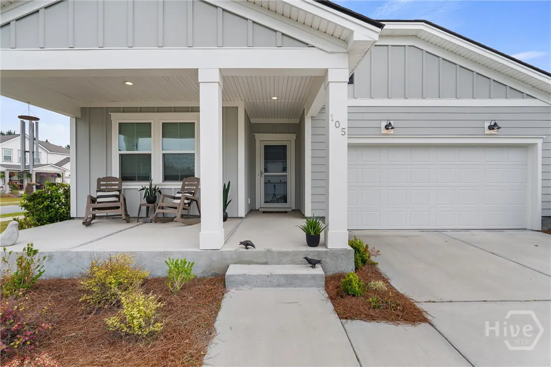 Exterior view of a gray house with a white garage door and porch. Two rocking chairs sit on the porch. A walkway leads to the front door.
