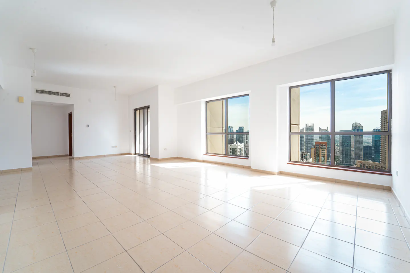 Bright, empty room with beige tile floor, white walls, and large windows showing a city skyline.