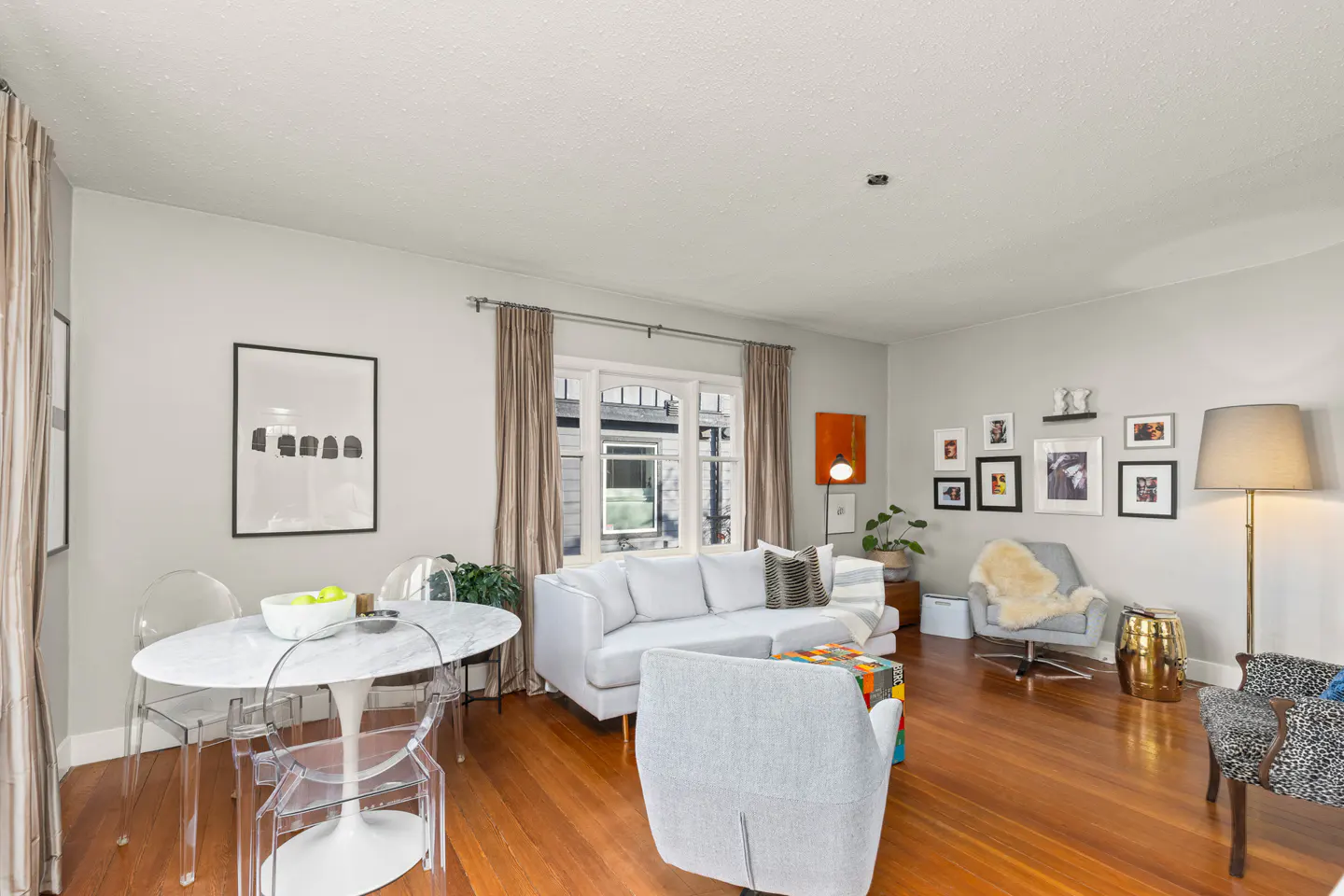 Bright living room with hardwood floors, white sofa, marble table, and gallery wall. Neutral tones with pops of color.