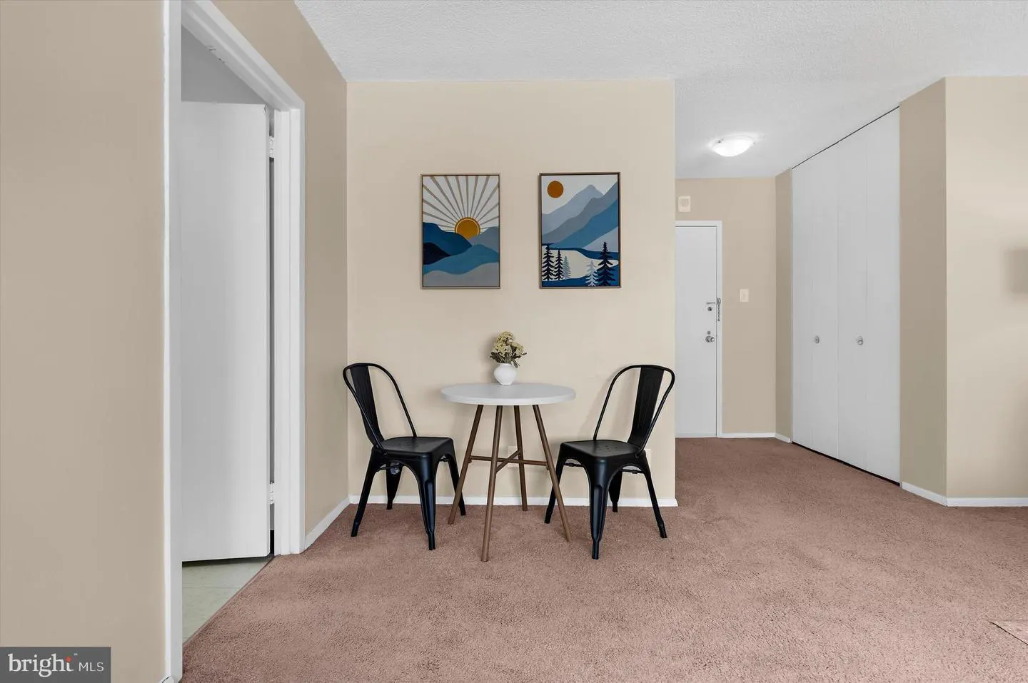 Interior view of a room with beige walls, pink carpet, a white table with two black chairs, and two framed landscape pictures.