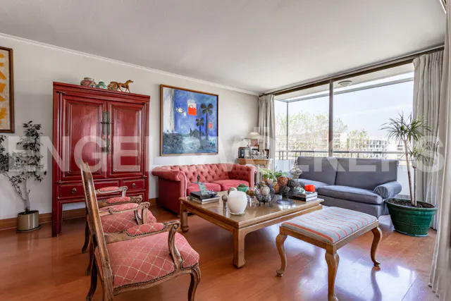 Living room with red armchairs, a red cabinet, a tufted red sofa, a grey sofa, and a wooden coffee table on wood floors.