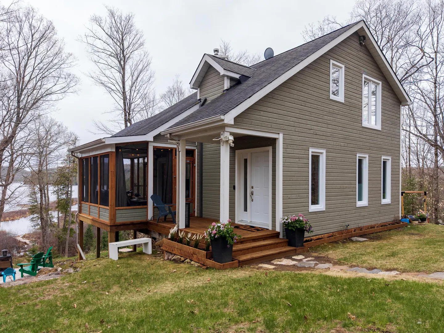 Exterior view of a two-story house with a screened-in porch, wood deck, and green lawn. The house is light green with white trim and a dark roof.