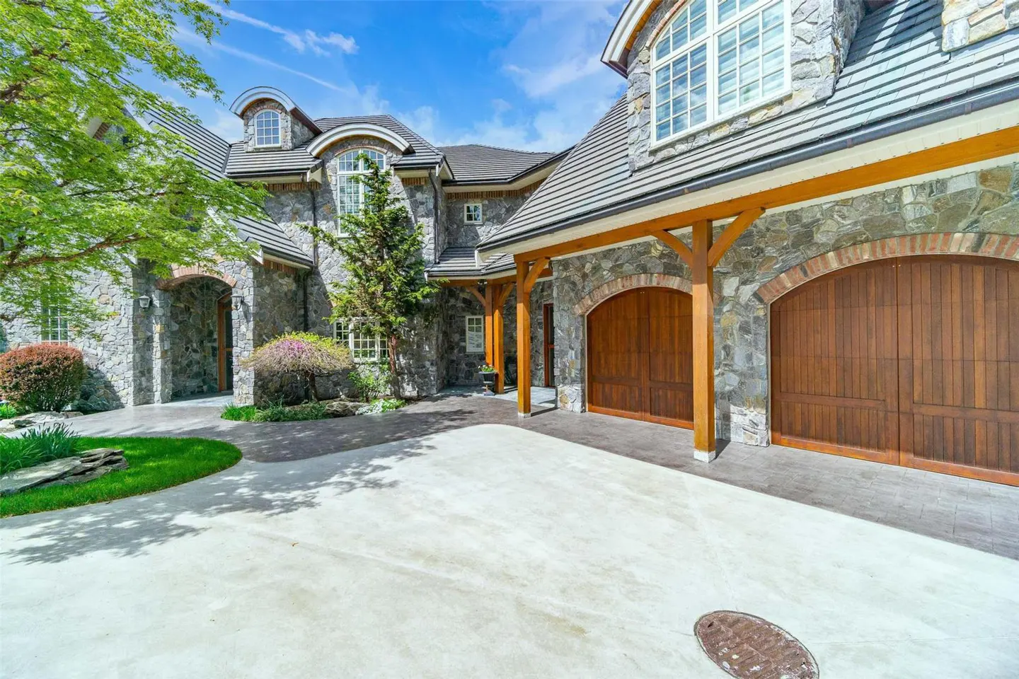 Exterior of a stone house with arched wooden garage doors and a concrete driveway.