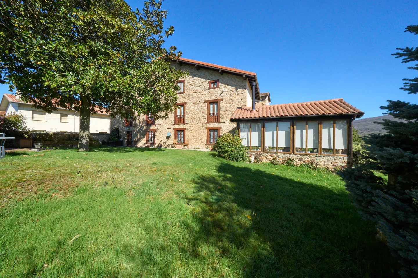 Exterior view of a stone house with a red tile roof and a green lawn on a sunny day.