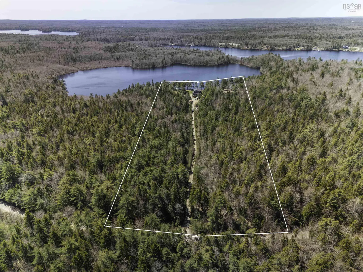 Aerial view of a wooded property outlined in white, leading to a lake. Trees are green and brown.