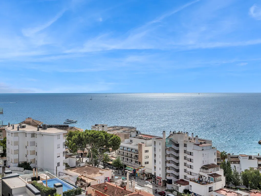 Ocean view of white buildings under a blue sky. Boats are visible on the water.