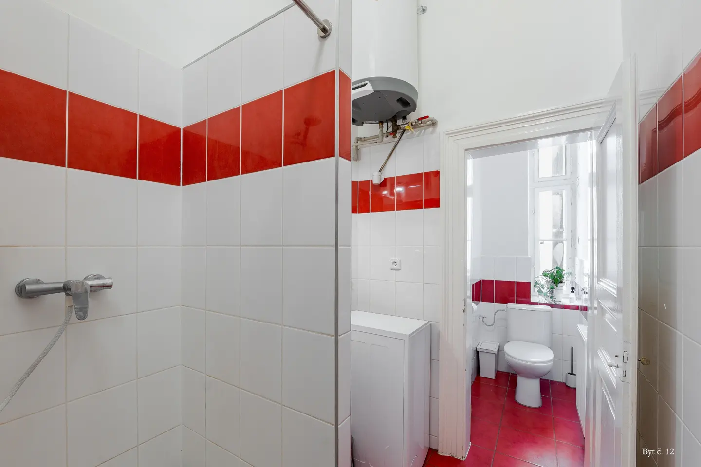 Bathroom with white and red tiled walls, a shower area, a water heater, a washing machine, and a toilet in the back.