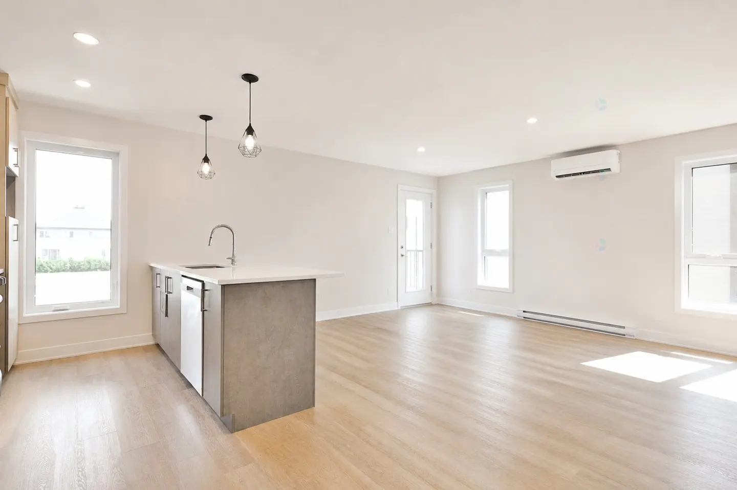 Bright, modern kitchen and living area with light wood floors, white walls, and a gray kitchen island with a white countertop.