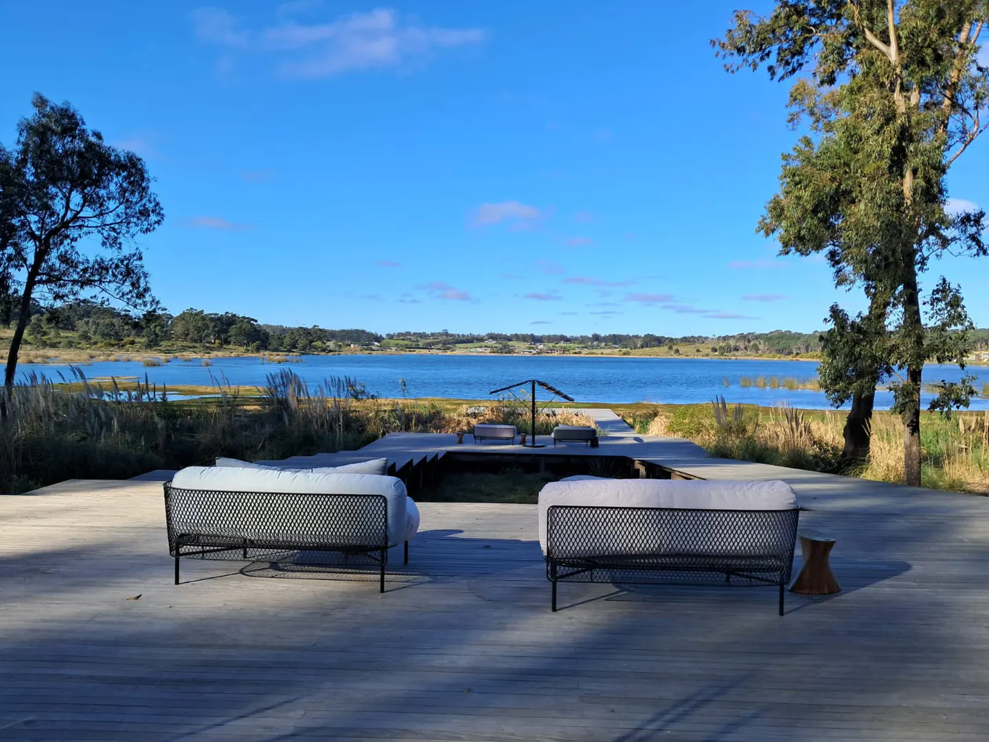 Outdoor seating area with two sofas on a wooden deck overlooking a blue lake under a clear sky.