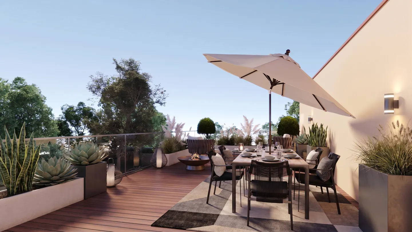 Outdoor patio with dining table, chairs, and umbrella on a wood deck. Planters with greenery line the edge, with a fire pit in the background.