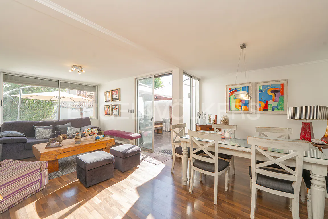 Bright open-plan living and dining room with hardwood floors, a grey sofa, wooden coffee table, and white dining set.