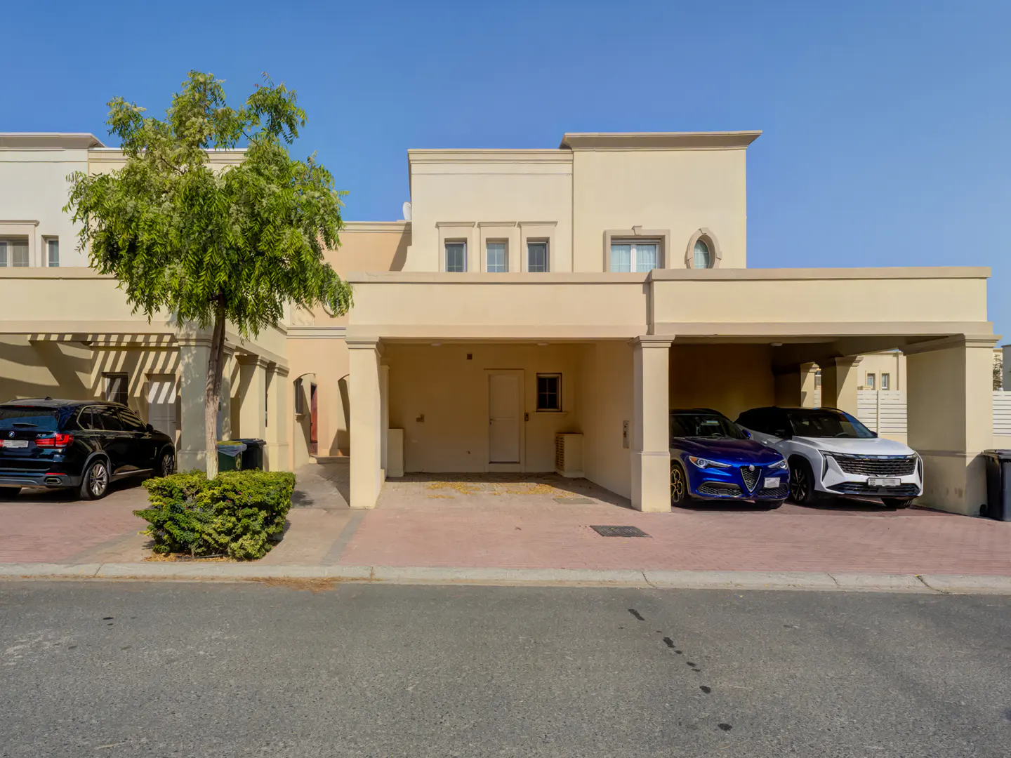 Beige two-story house with two carports. A black SUV is parked on the left, and a blue and white car are parked on the right.