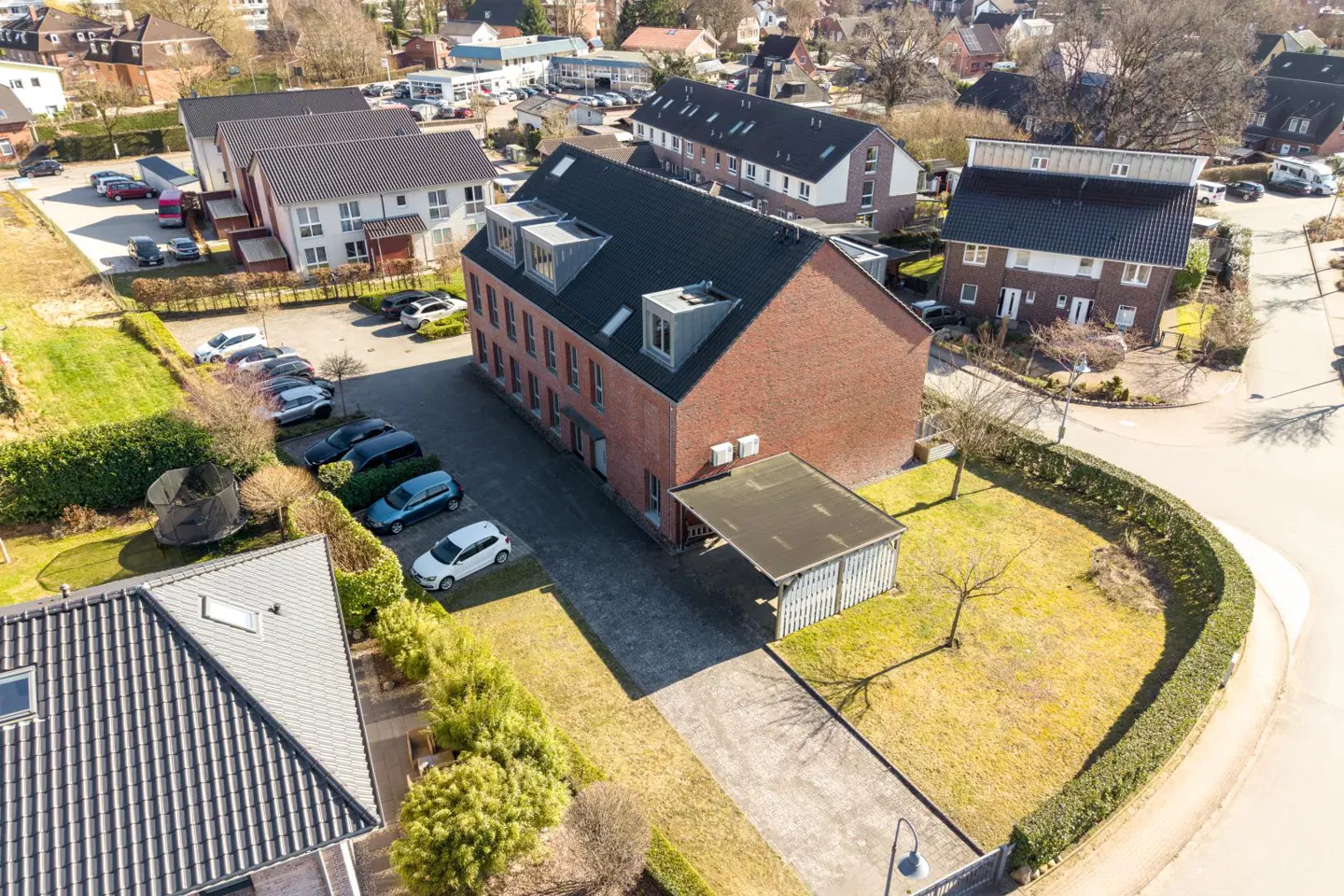 Aerial view of a red brick apartment building with a parking lot, carport, and surrounding residential neighborhood.