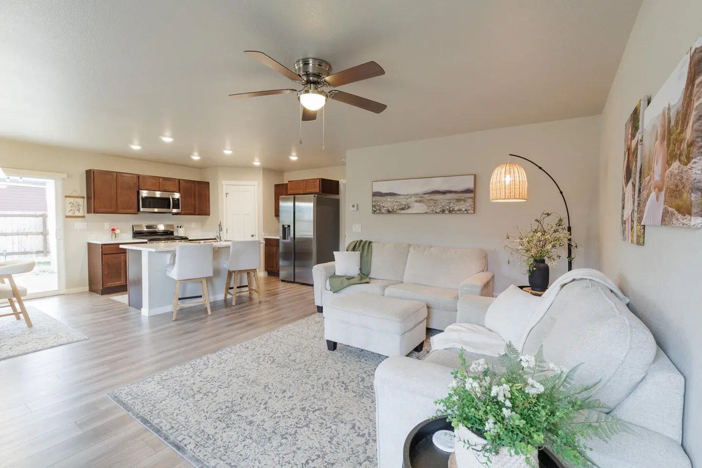 Open-concept living space with a kitchen, island with stools, and a living room with white sofas and a ceiling fan.