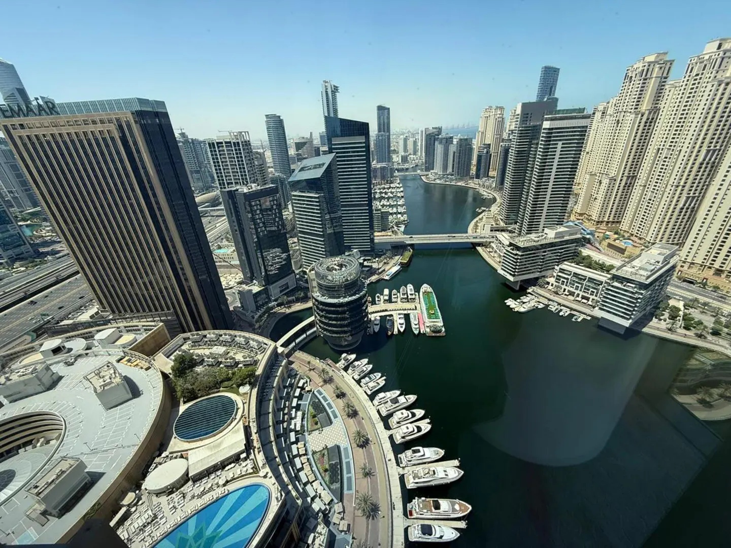 Aerial view of Dubai Marina with skyscrapers, yachts, and a blue swimming pool on a sunny day.