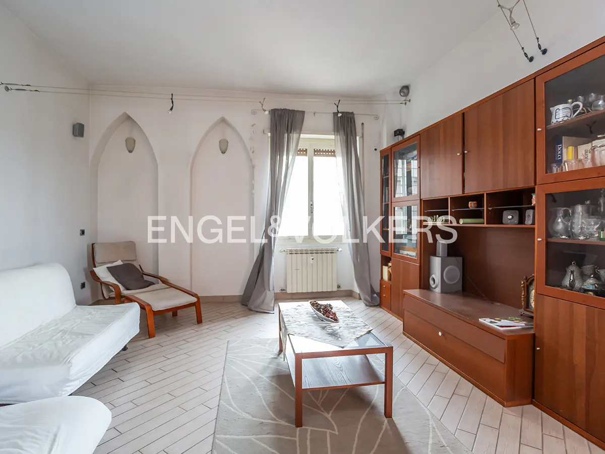 Bright living room with white walls, light wood floors, and a large brown built-in cabinet. A white sofa and chaise lounge sit near arched wall niches.