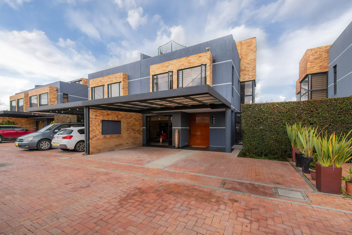 Exterior view of modern townhouses with brick and gray facades, carports, and a brick driveway.