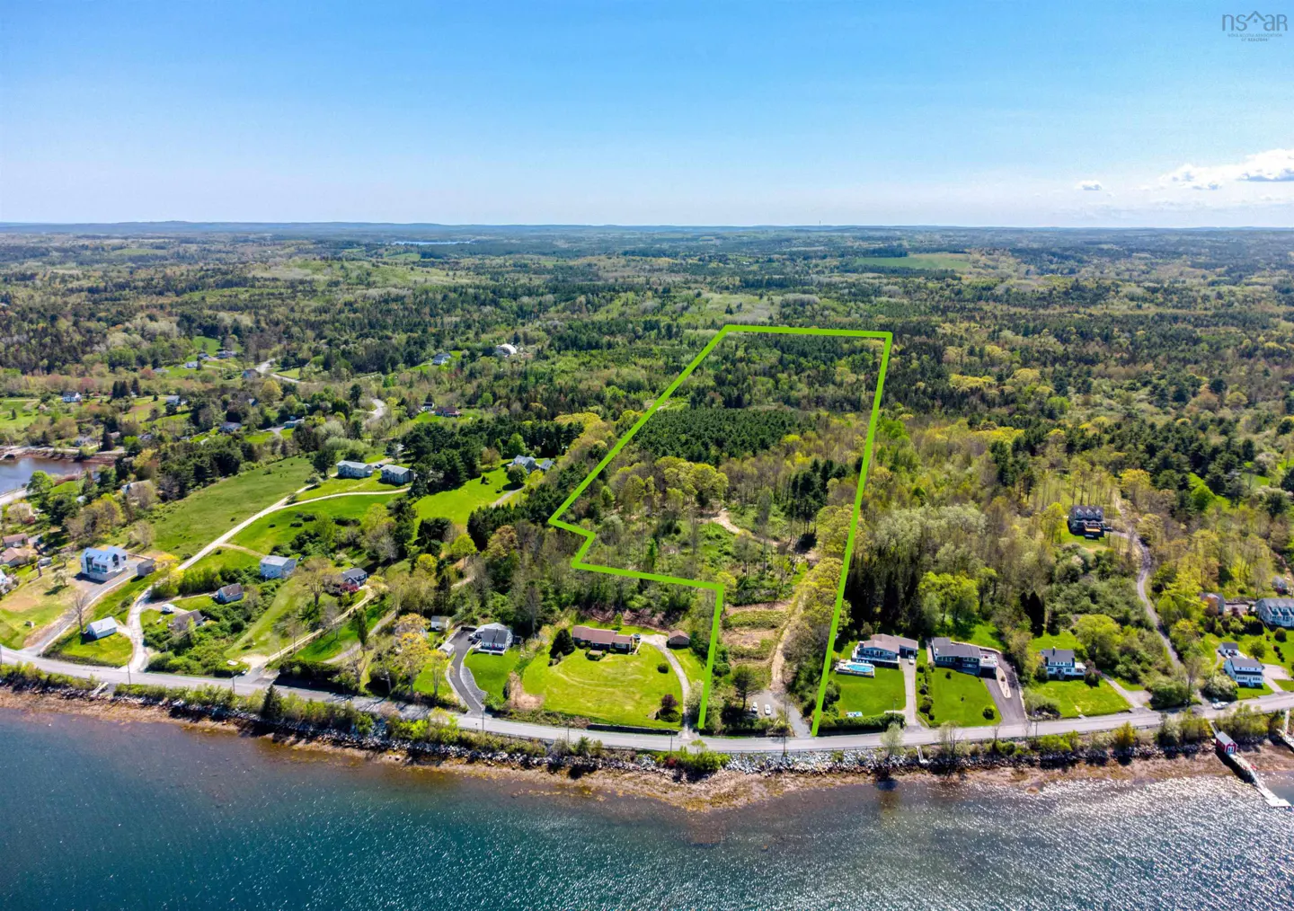 Aerial view of a large, green-bordered property with trees, houses, and waterfront on a sunny day.