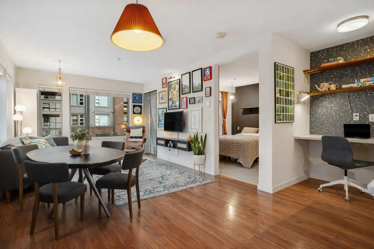 Open-concept apartment with wood floors, a dining table, living area, bedroom, and a desk with shelves.