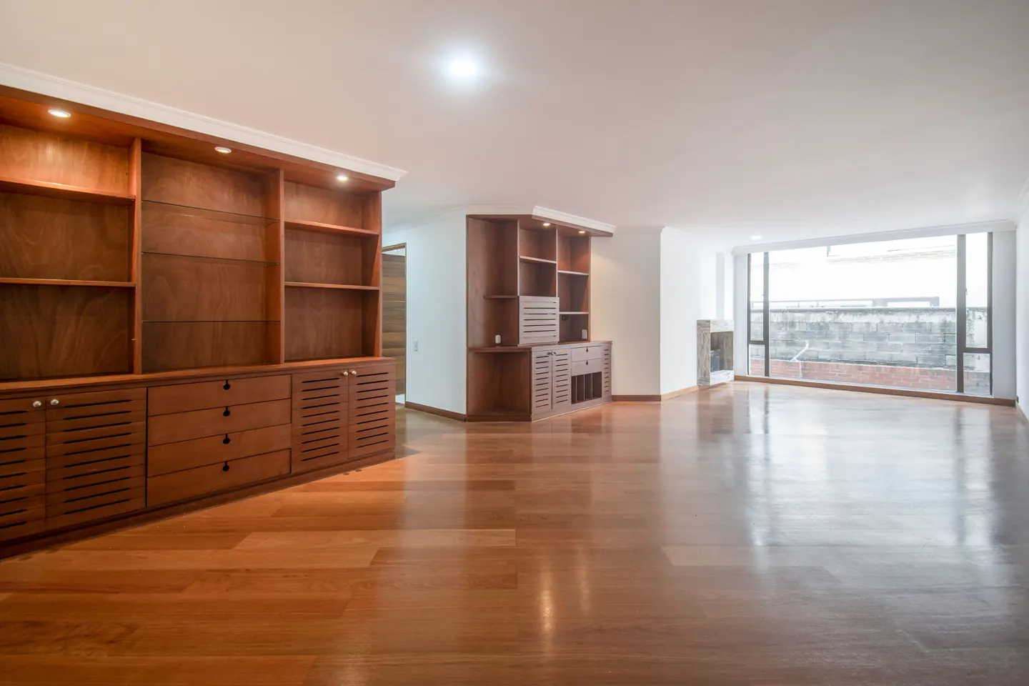 An empty living room with hardwood floors, built-in wooden cabinets, and a large window.