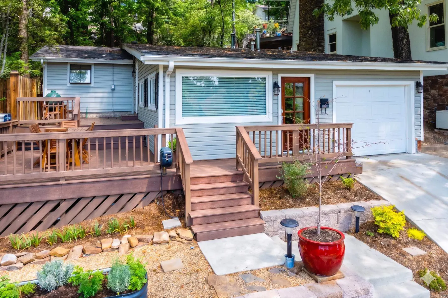 Exterior of a light blue house with a brown door, white garage door, and a wooden deck with outdoor furniture.