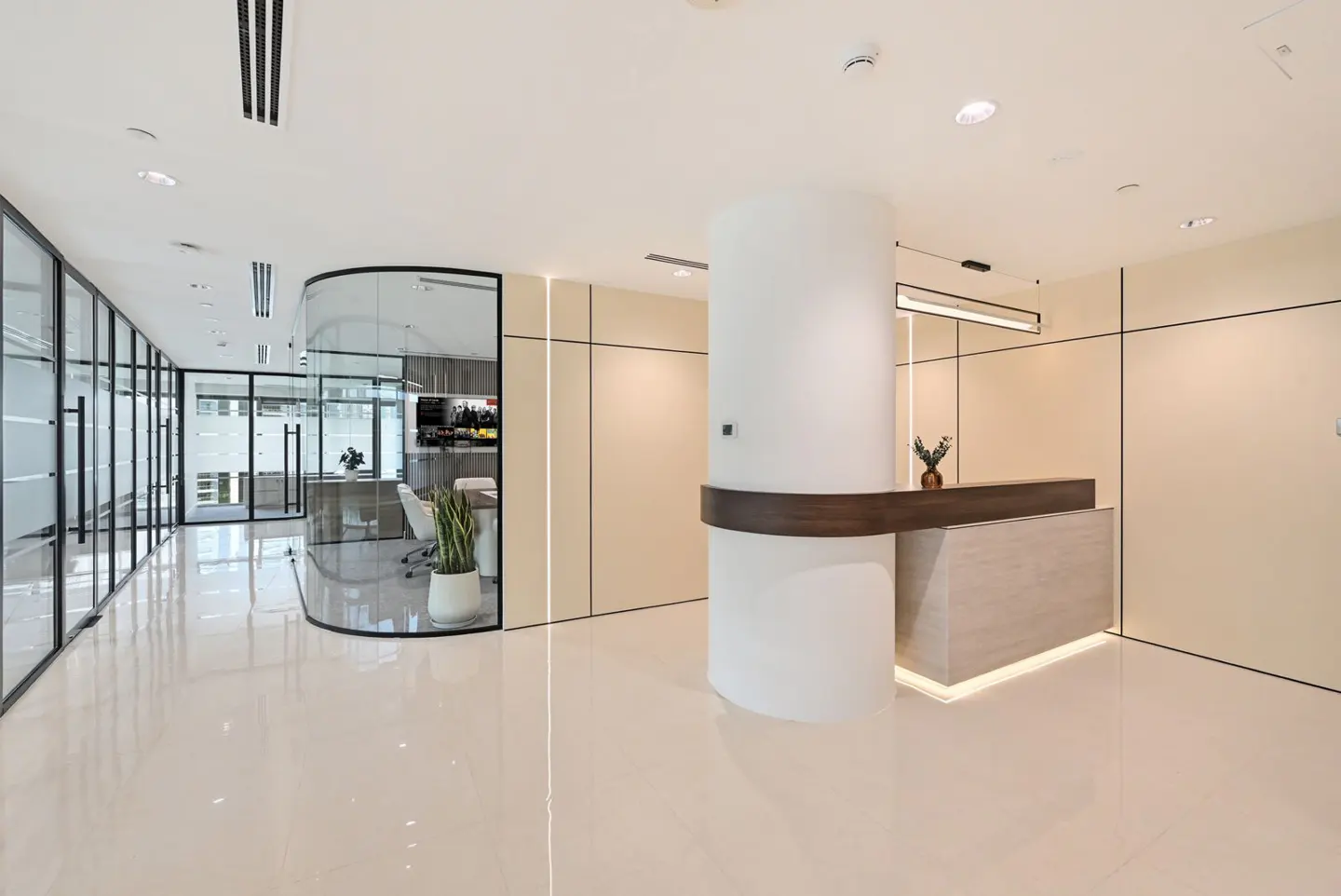 Bright, modern office lobby with a white reception desk, glass-walled offices, and shiny floors. A plant sits on the desk.