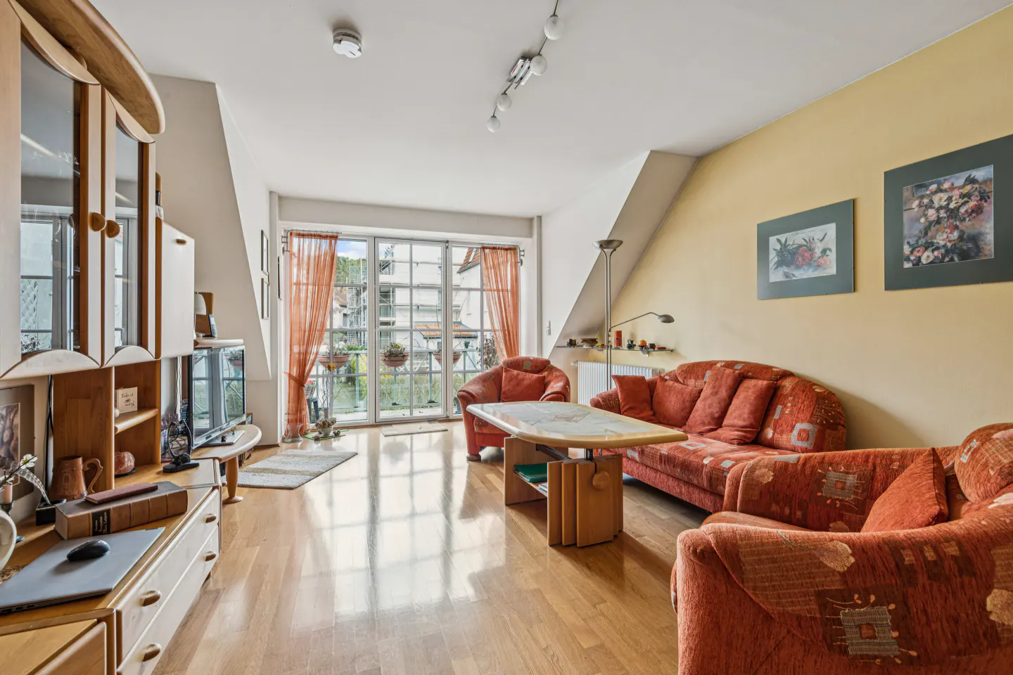 Living room with hardwood floors, orange patterned sofa and chairs, and a balcony with orange curtains.
