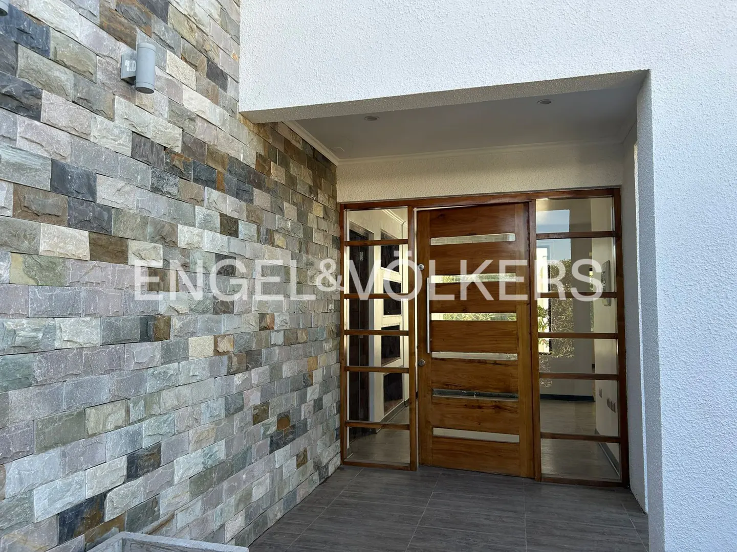Exterior view of a modern home with a stone wall and a wooden front door with glass panels.