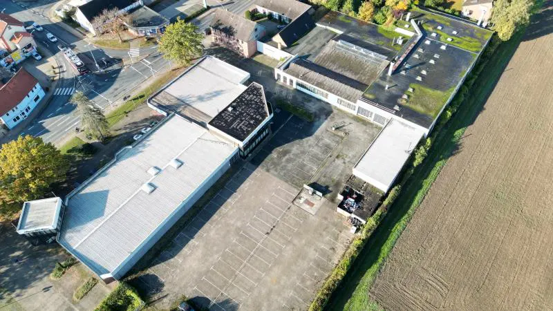 Aerial view of a large, low, commercial building with a gray roof and empty parking lot.